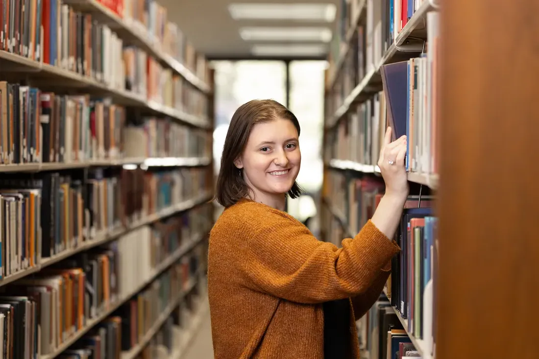 学生 inside of library choosing book from shelf.